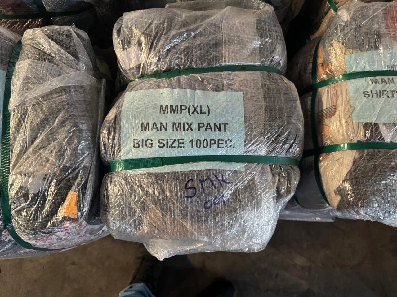 A wrapped clothing bale with a category label and green straps