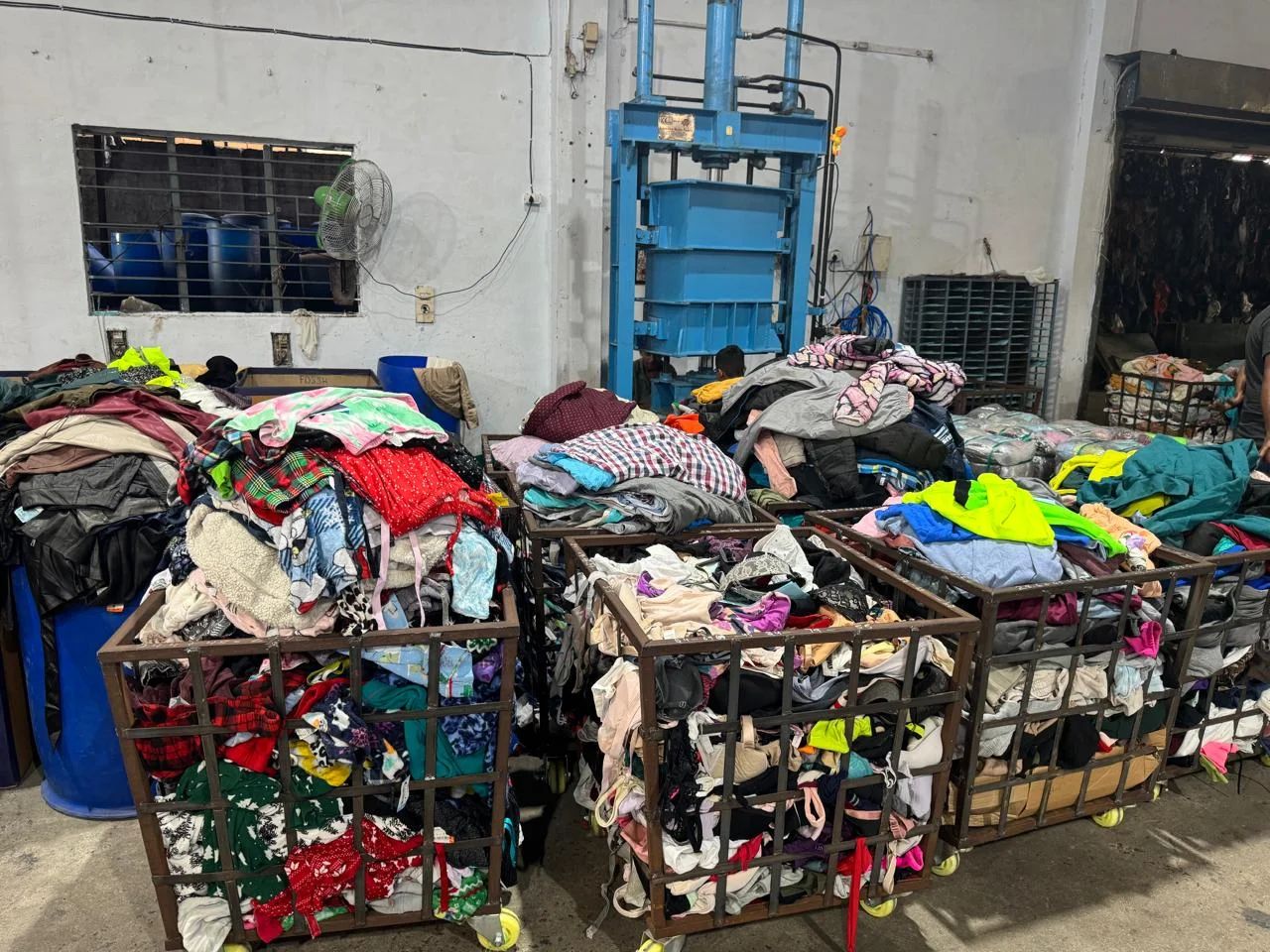 Mixed garments in cages beside a textile baling press